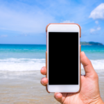 photo d'une mail tenant un téléphone portable, sur une plage devant la mer